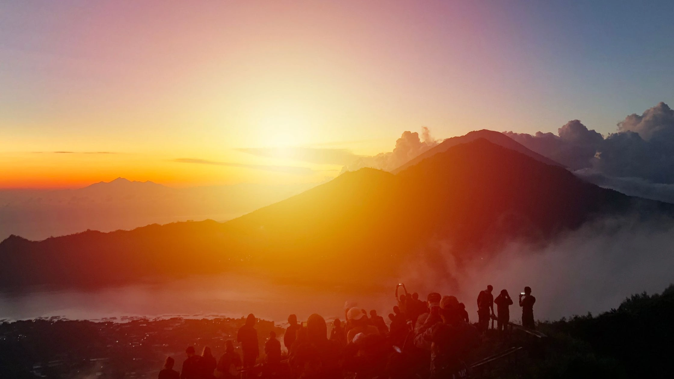 Hikers ascend the slopes of the Batur volcano at dawn, silhouetted against the rising sun. This photo illustrates the challenging yet rewarding experience of a volcano hike in Bali.