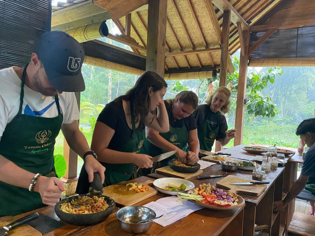 Participants at Bali Farm Cooking School pick fresh ingredients from an organic garden. This photo captures the Bali Farm Cooking School experience in Ubud. People are gathering fresh produce in an organic garden, emphasizing its farm-to-table approach.