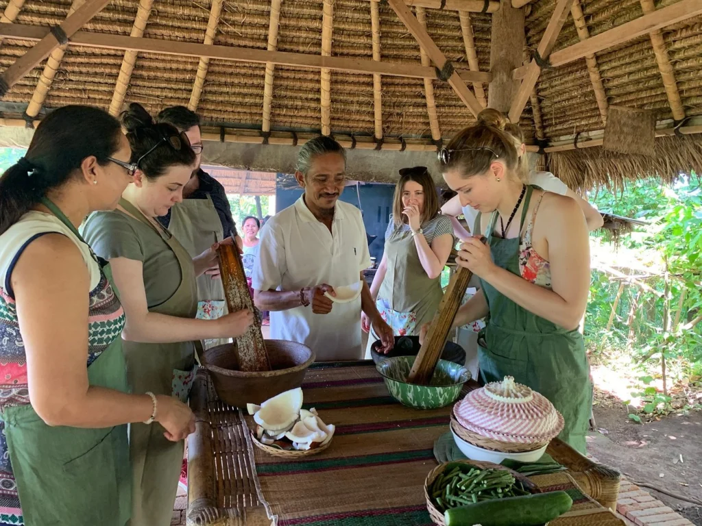 A group explores a local market for ingredients during a Green Kitchen Bali cooking tour. This picture shows a Green Kitchen Bali cooking tour. Participants are at a vibrant local market, gathering fresh ingredients, highlighting the comprehensive tour aspect before cooking.
