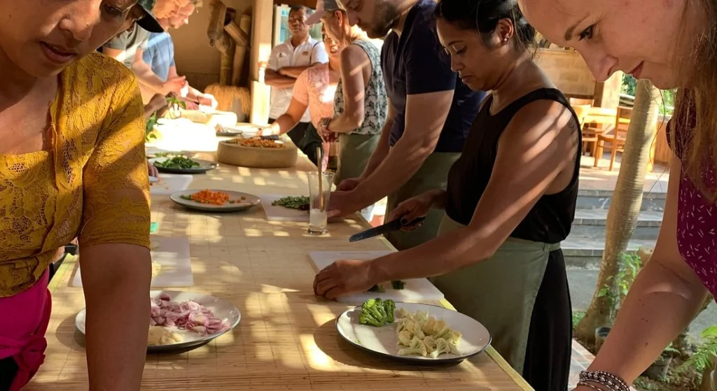 Students at Paon Bali learn to cook authentic dishes in a traditional kitchen. This image shows a Paon Bali Cooking Class in Ubud. Participants are actively cooking in a traditional Balinese kitchen, highlighting the authentic, hands-on experience.
