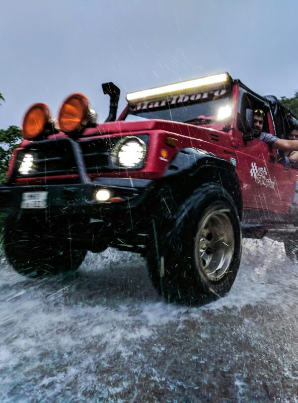 Dynamic shot of a red jeep navigating a rugged terrain during a rainstorm, capturing the thrill of off-road driving.