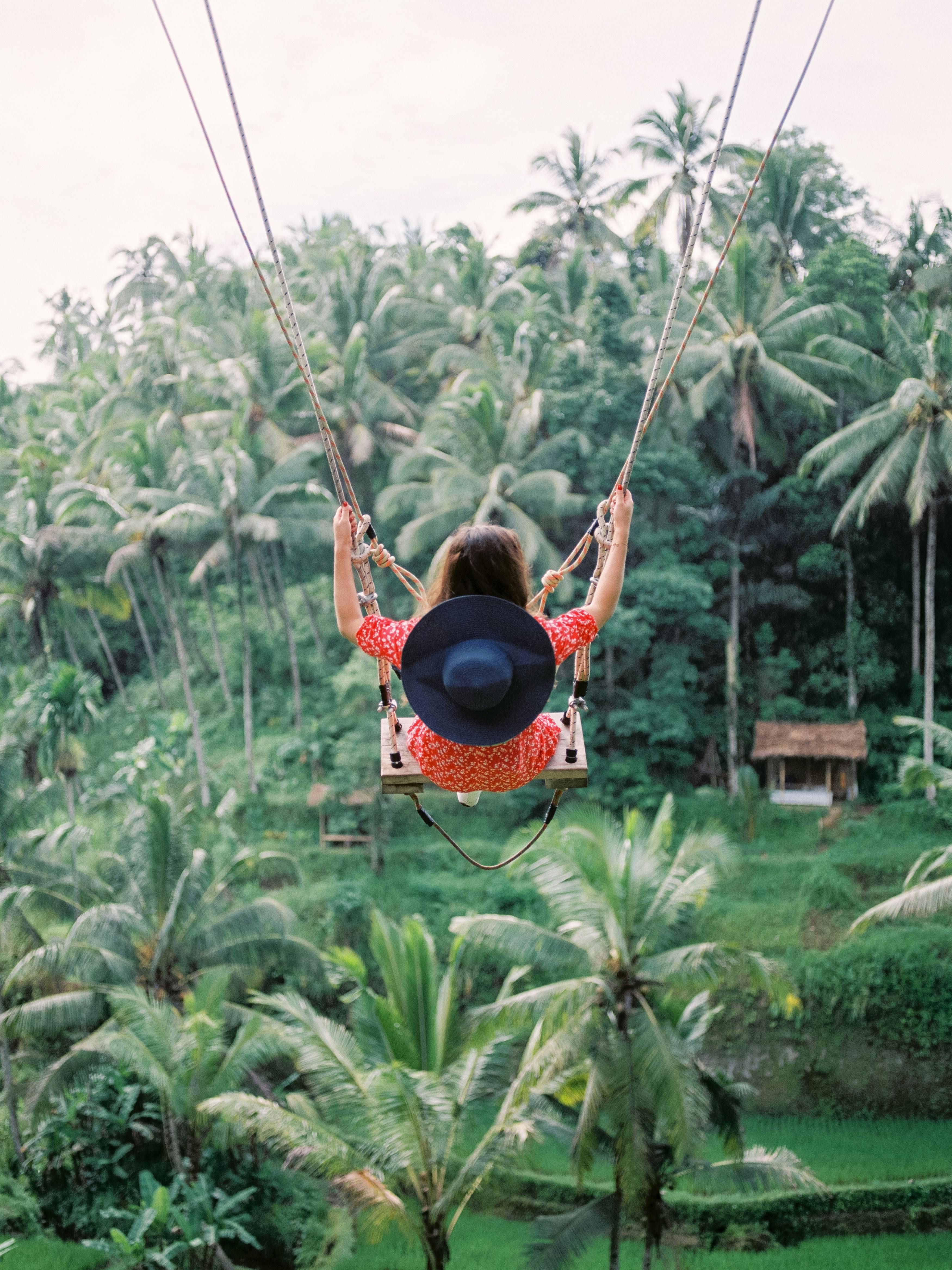 A woman swings high above the lush tropical jungle in Ubud Bali, showcasing the vibrant scenery and adventure, 7 day trips in Ubud.