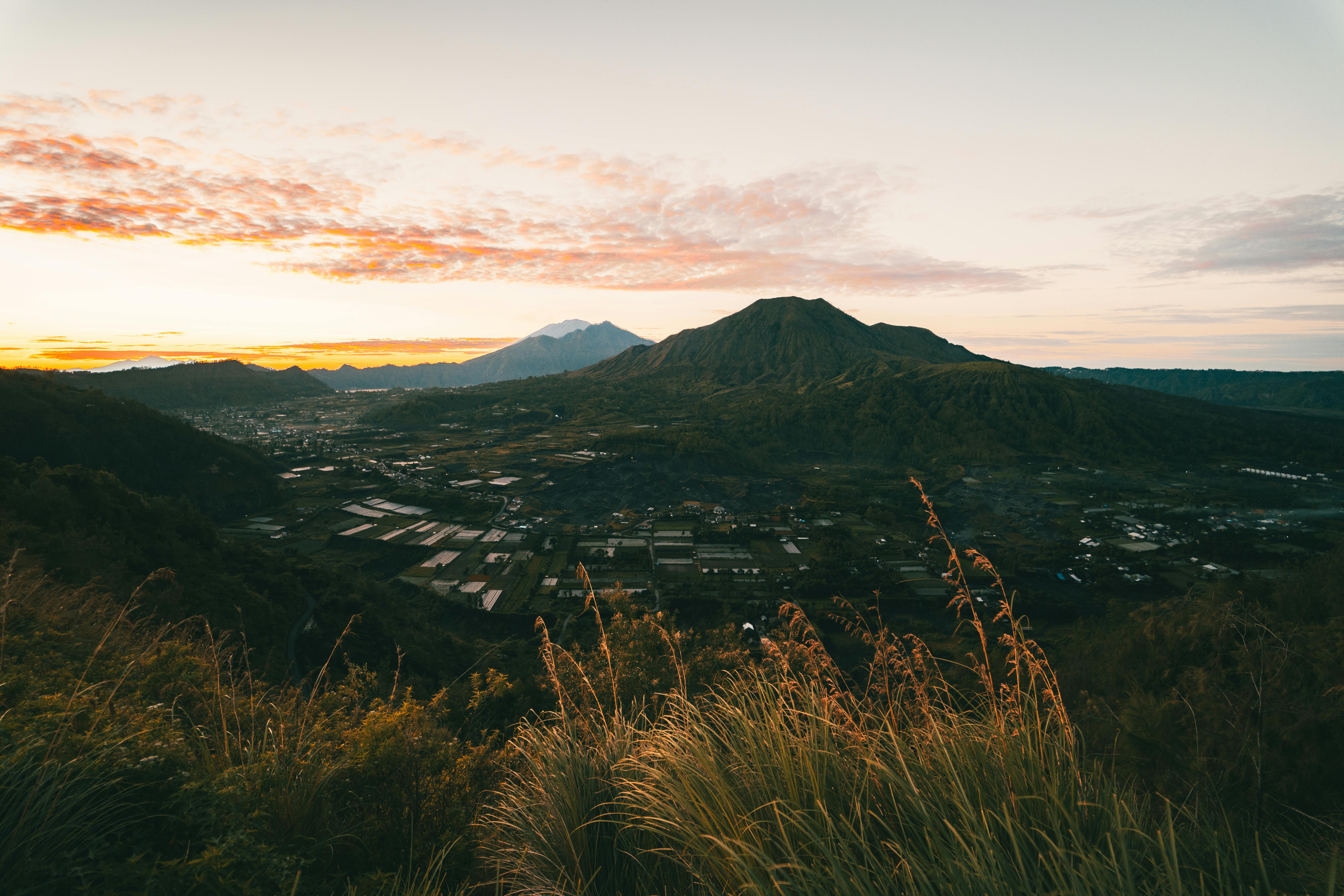 Sunrise view of Mount Batur and surrounding landscape in Bali, Indonesia, featuring lush vegetation and distant mountains.