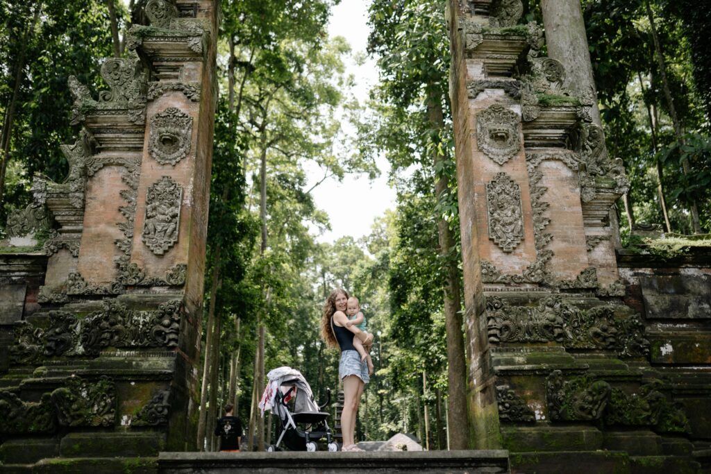 A mother and child stand by an ancient temple gate surrounded by lush greenery.