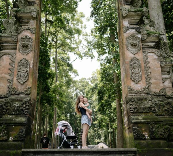 A mother and child stand by an ancient temple gate surrounded by lush greenery.
