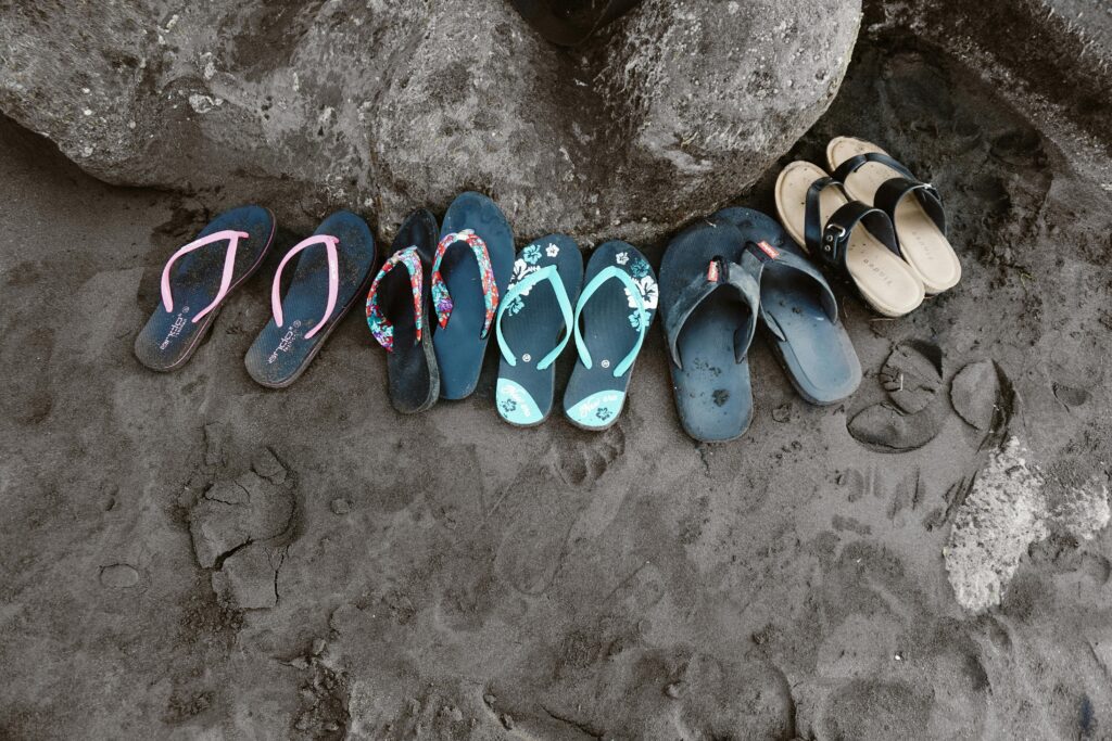 A collection of vibrant flip flops kids and family left on the sand in Bali, Indonesia, depicting a casual beach vibe.