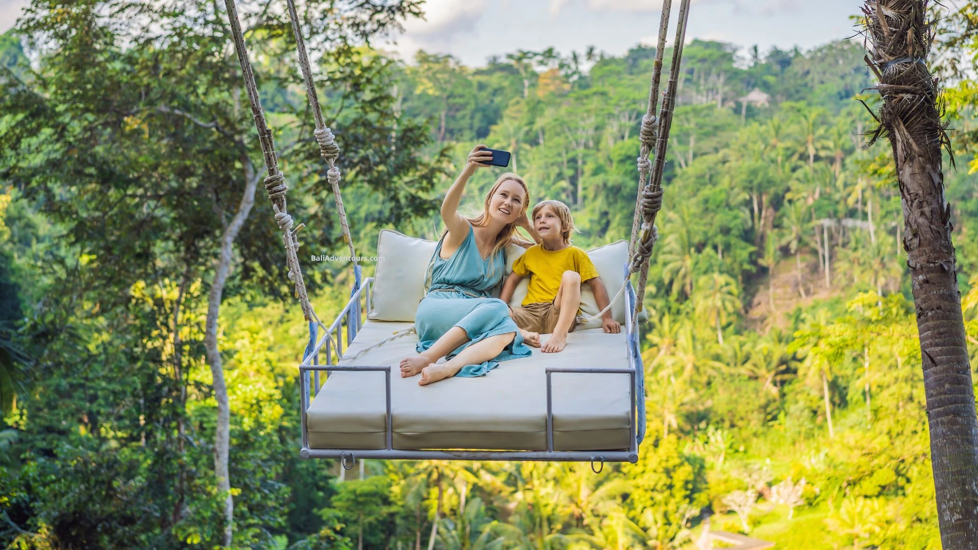 A mother and her child sitting on a swing in Ubud, taking photos together. They enjoy the view and the peaceful nature of Bali.