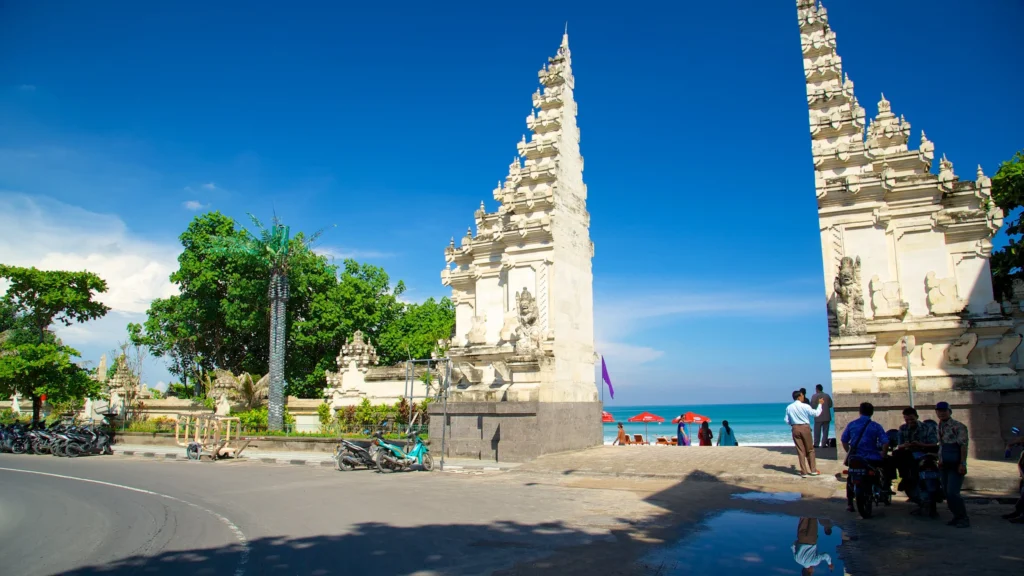 Bustling beach area in Kuta or Legian with people, surfboards, and beachfront cafes, showing its energetic and tourist-heavy environment.