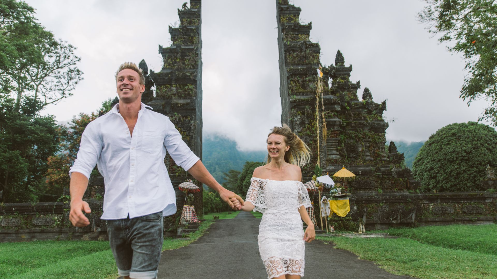 A married couple takes photos in front of a Balinese gate. They enjoy their holiday and the cultural scenery.