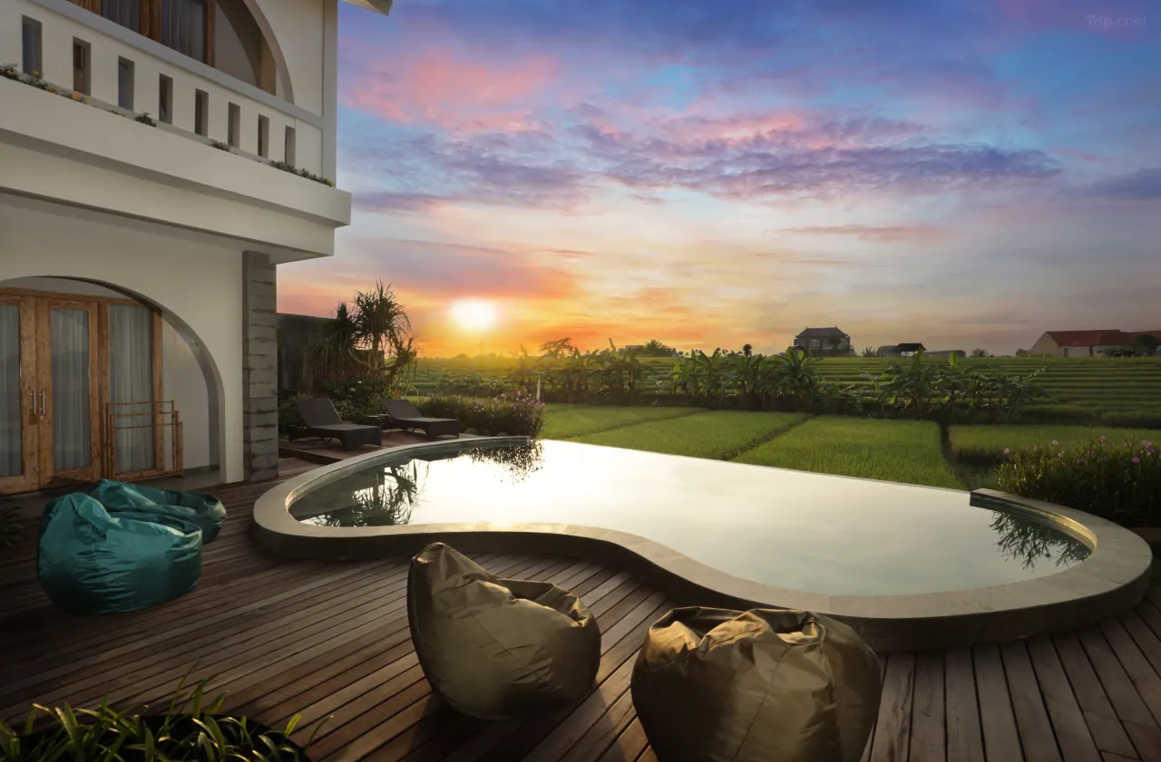 A luxurious resort villa in Ubud with a private pool and a unique, natural exterior design that blends with the surroundings. The villa has a serene view of a rice paddy field during sunrise, with the golden light reflecting off the water.