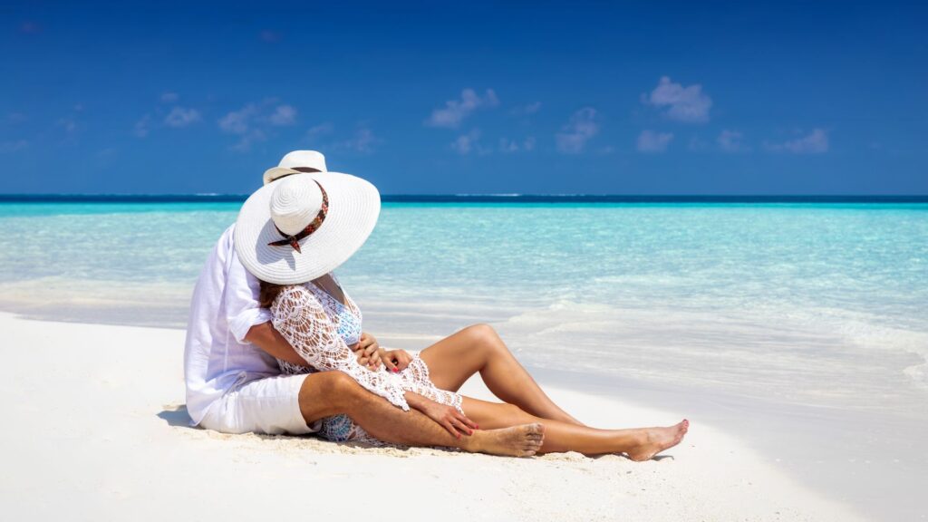A couple sit down on the beach hand in hand along a quiet Bali beach at sunset, representing a relaxed honeymoon vibe.