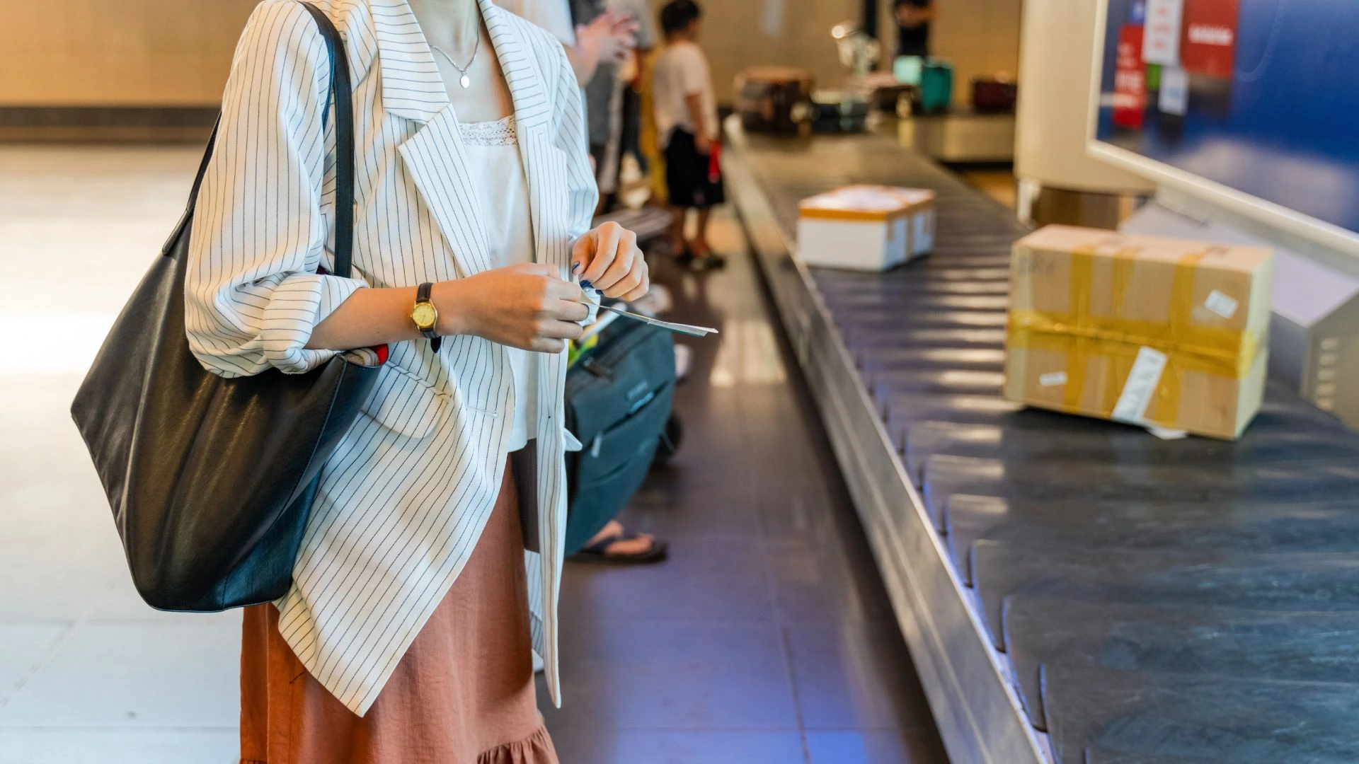 A chaotic scene in the baggage claim area of Bali's Ngurah Rai International Airport. The image shows a tourist struggling with luggage while surrounded by unofficial "helpers" who are aggressively offering to assist with bags for an undisclosed fee, representing the baggage helper scam.