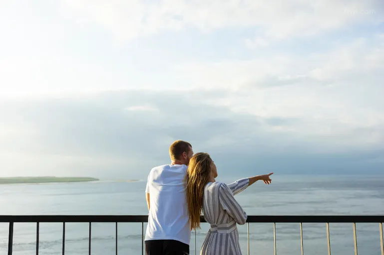 A couple is enjoying a beautiful ocean view from the balcony of their luxurious hotel room.