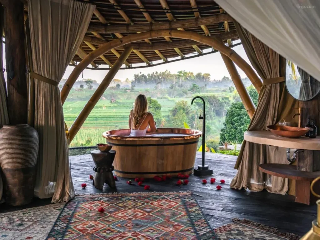 A female tourist is enjoying the natural scenery of Bali from a hammock-like net in front of her luxurious villa room. The room features a natural wooden interior design.