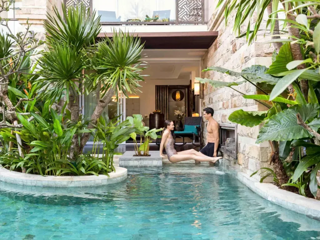 A newlywed couple enjoys their honeymoon in a private pool at a luxury hotel in Bali. The couple is seen relaxing in the water, with a romantic and serene atmosphere.
