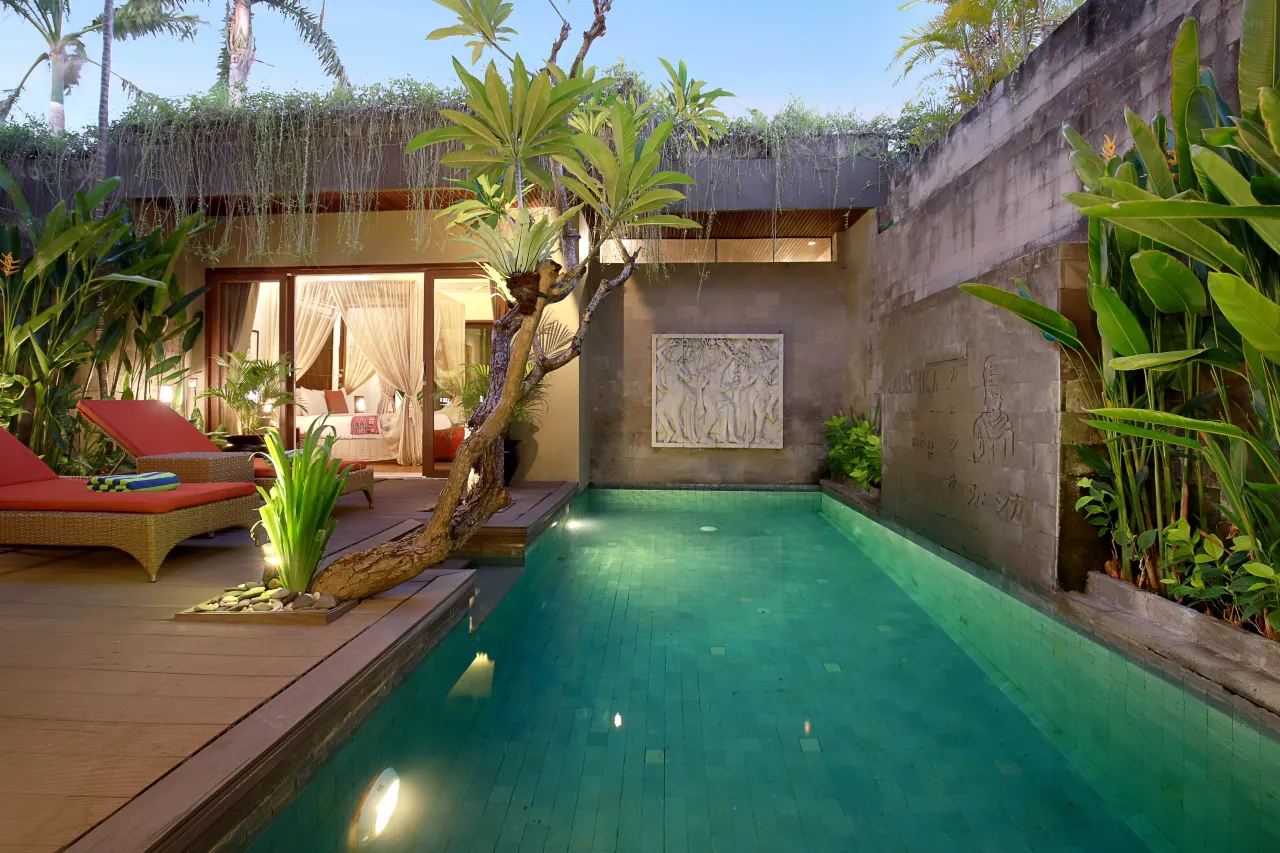 A luxurious resort villa nestled in the lush jungle of Ubud. The villa features a private infinity pool that overlooks a dense forest. Its unique exterior architecture is built with natural materials like wood and stone, and is designed to blend seamlessly with the tropical landscape.