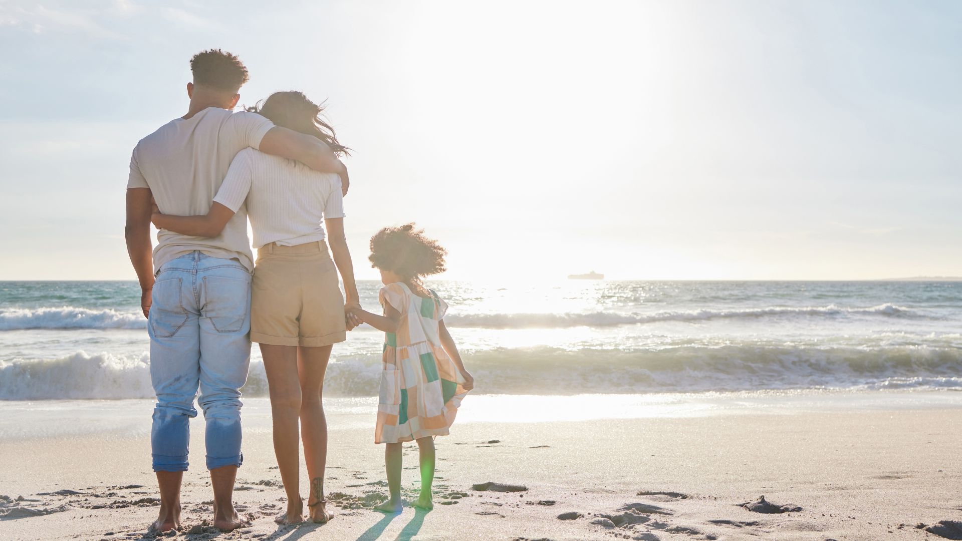 A mother, father, and young daughter standing together facing the beach in Bali.