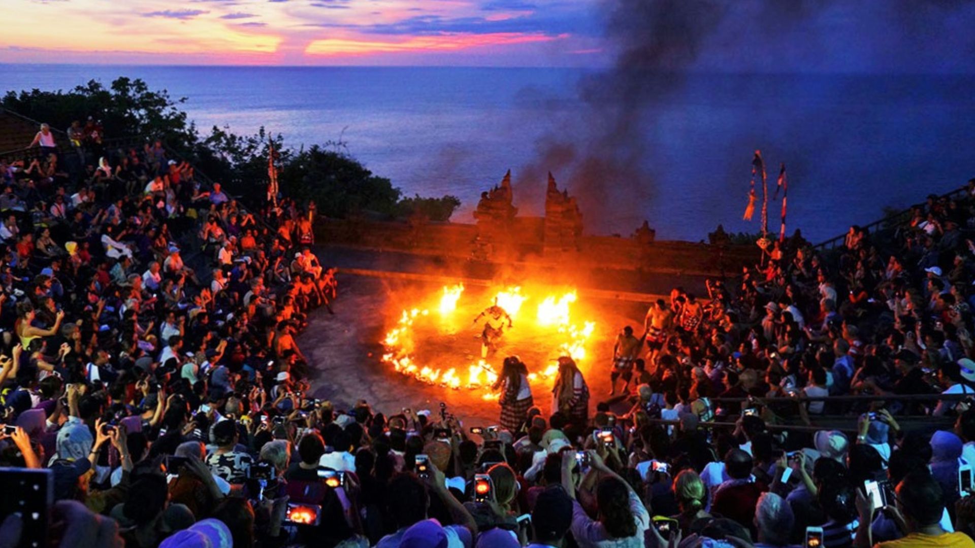 A crowd watching the famous Kecak dance performance in Uluwatu. The audience enjoys the show against a dramatic sunset backdrop.