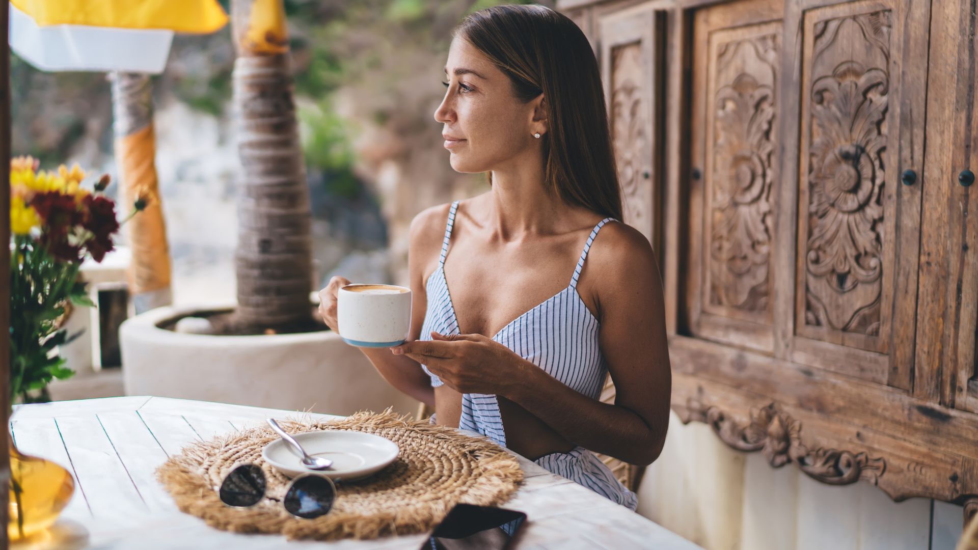A woman sipping a cup of Bali coffee at a nature café. She enjoys the peaceful atmosphere and beautiful view.