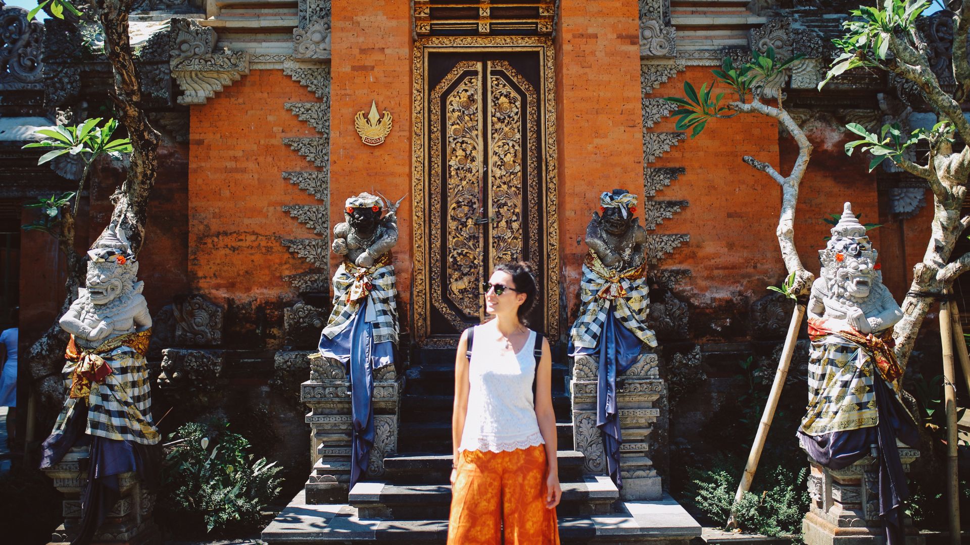 A female tourist wears a modest blouse and a Balinese sarong at a popular attraction. She poses respectfully while enjoying the cultural site.
