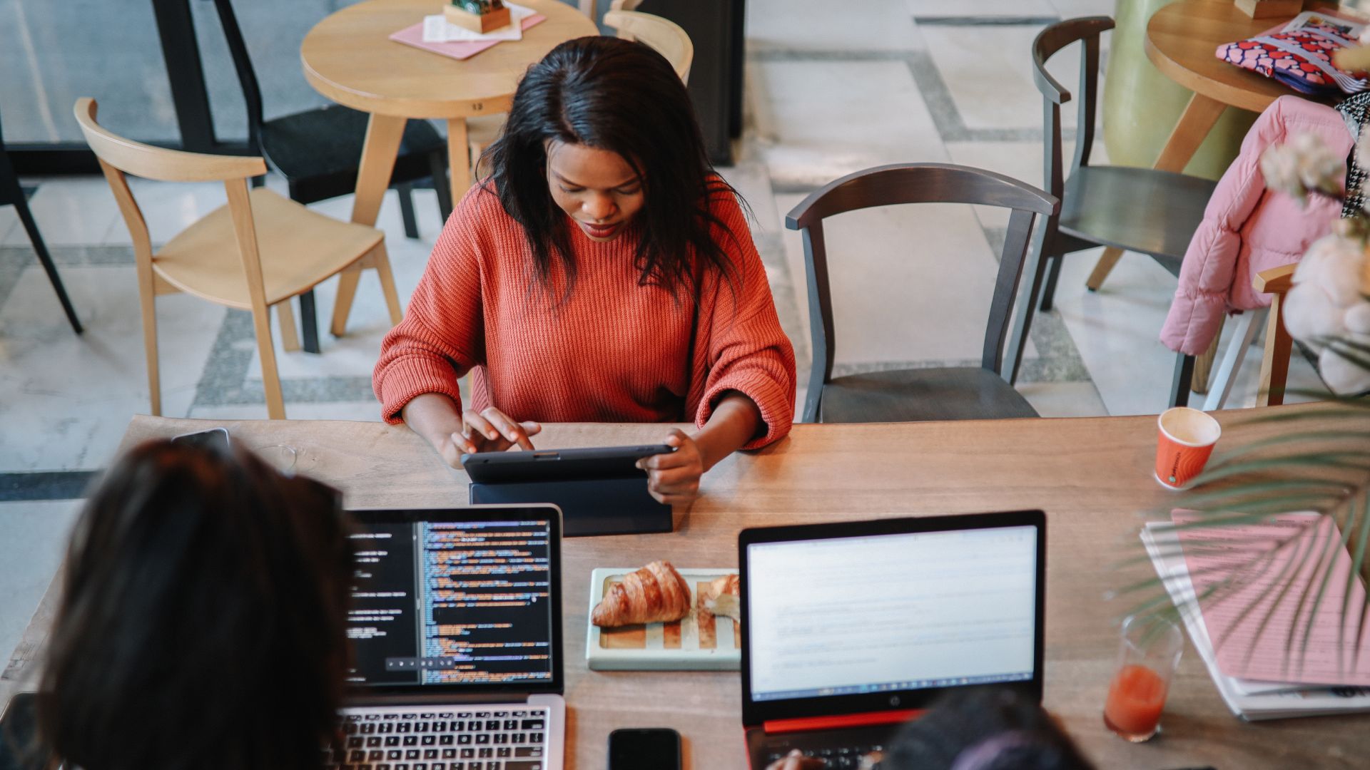 Several digital nomads work remotely in a Bali coworking space with their ordered meals on the table. Laptops, notebooks, and drinks sit beside the food.