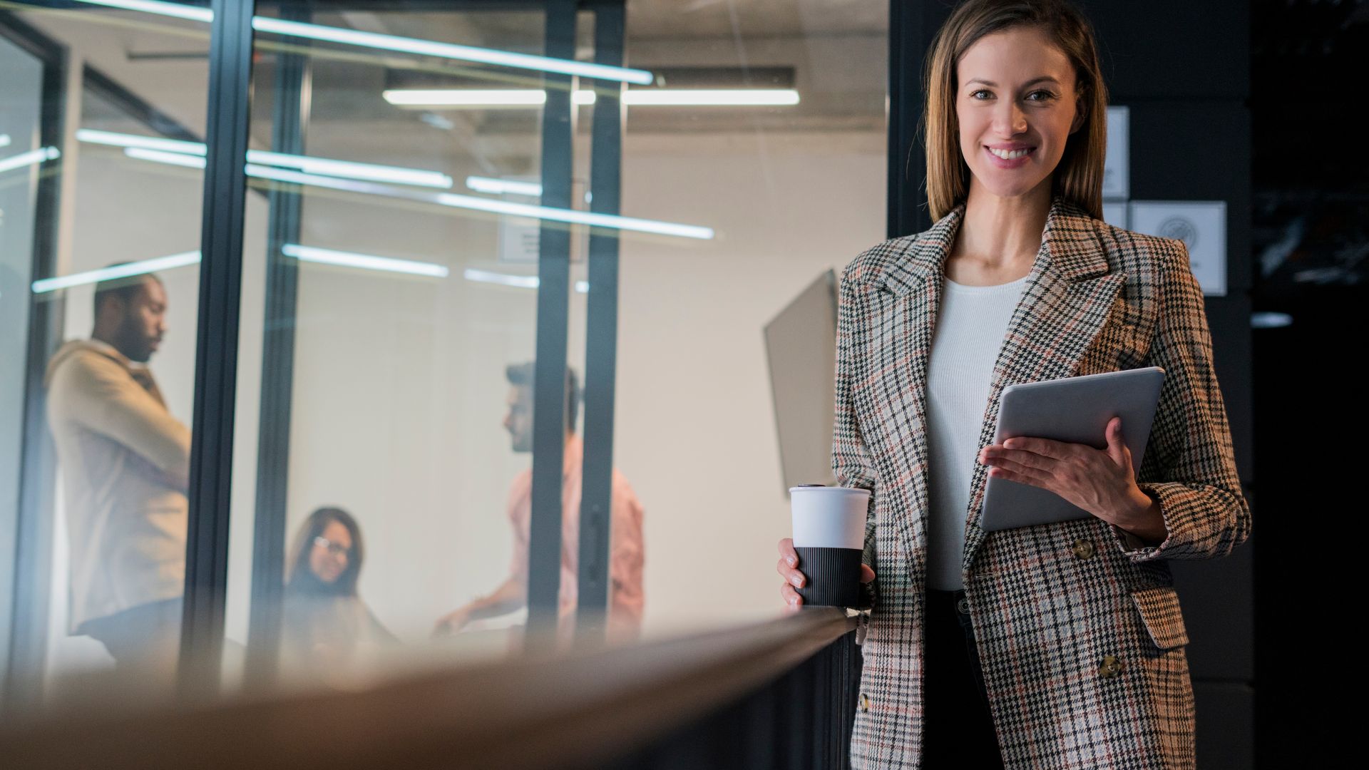 A foreign woman in Bali shares business tips at a coworking space after a client meeting. She holds a notebook and speaks near open desks.