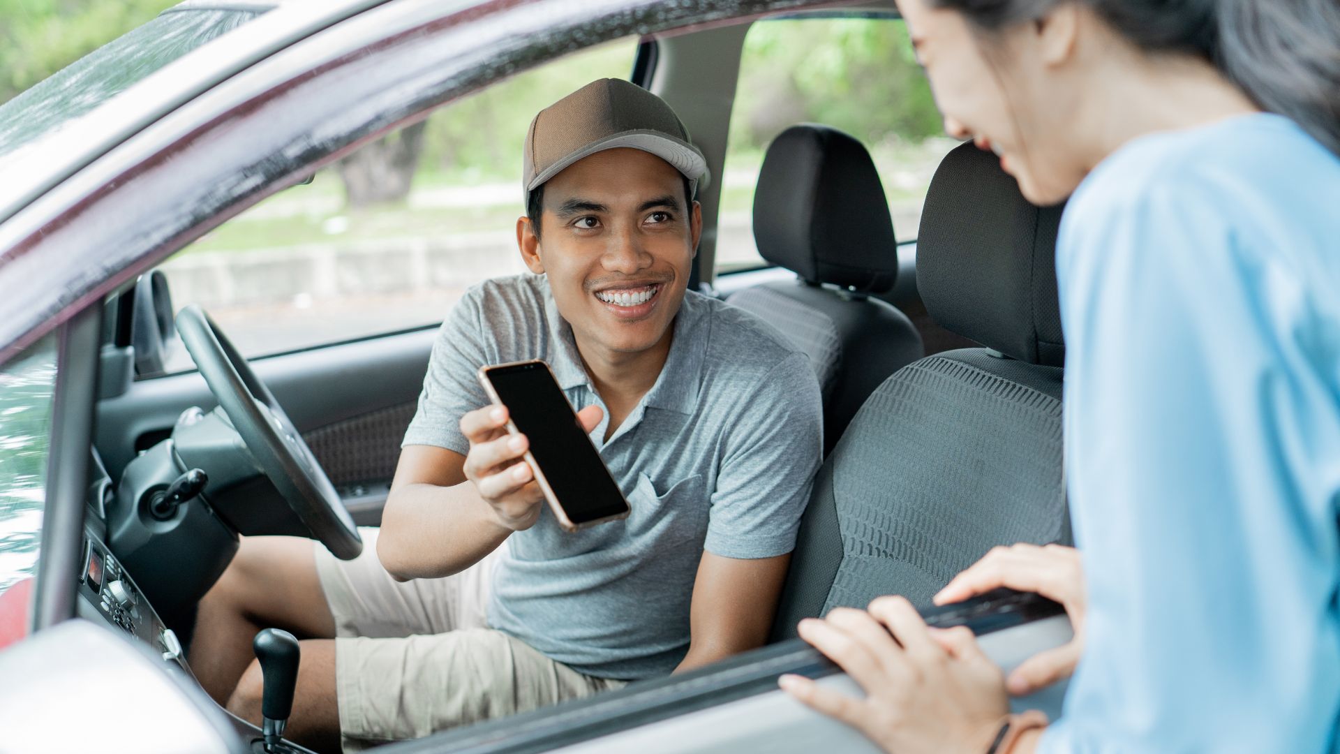 An online car driver in Bali showing the trip fare on the app to a tourist passenger. The screen helps the traveler know the price before the ride.