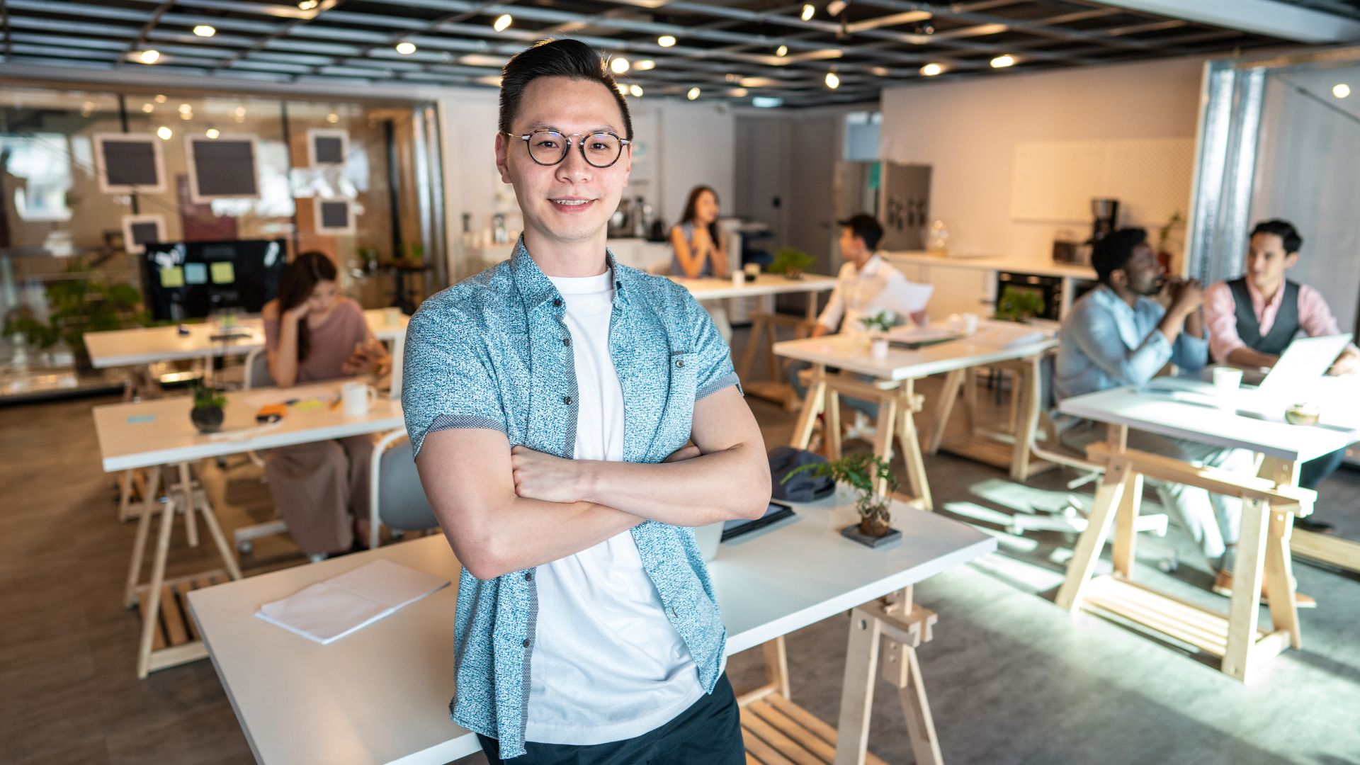 A business owner in Bali smiles inside the office with staff. Desks and computers show a busy but friendly workspace.