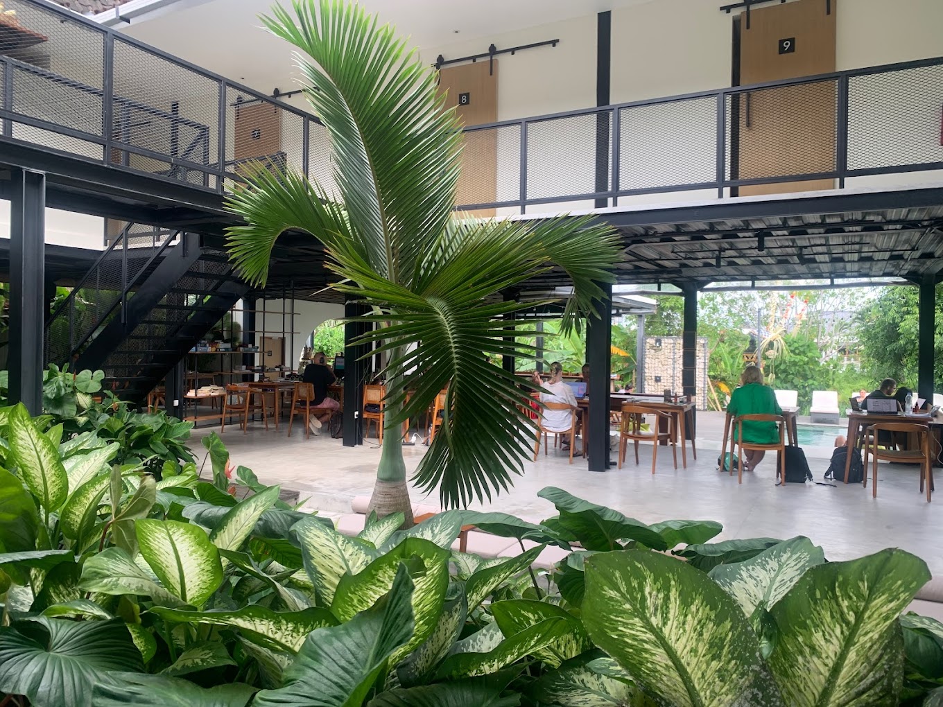 A scenic view inside Tribal Bali café that also functions as a coworking space in Canggu, Bali. Large windows, green plants, and quiet seating invite focused work.