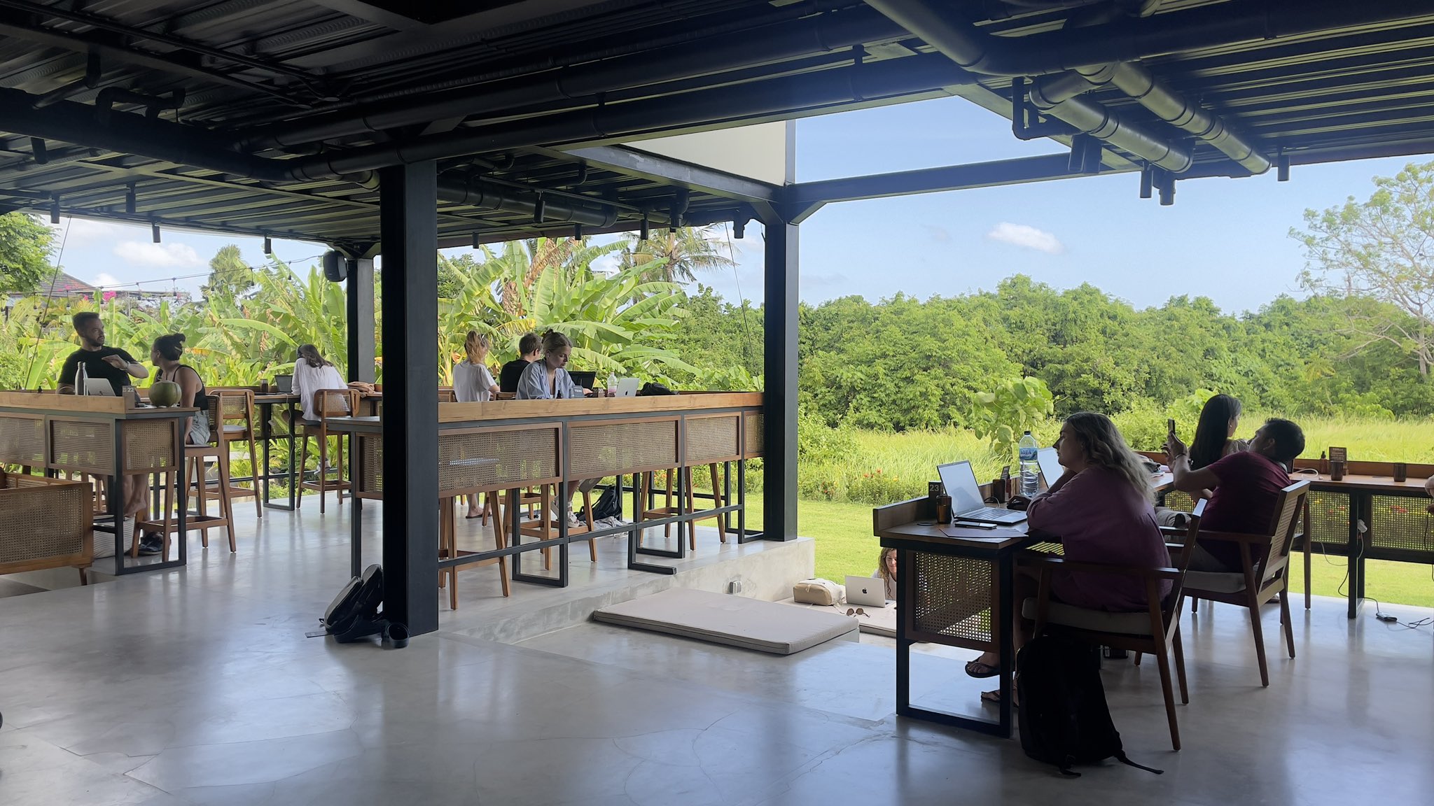 A scenic view inside Tribal Bali café that also functions as a coworking space in Canggu, Bali. Large windows, green plants, and quiet seating invite focused work.