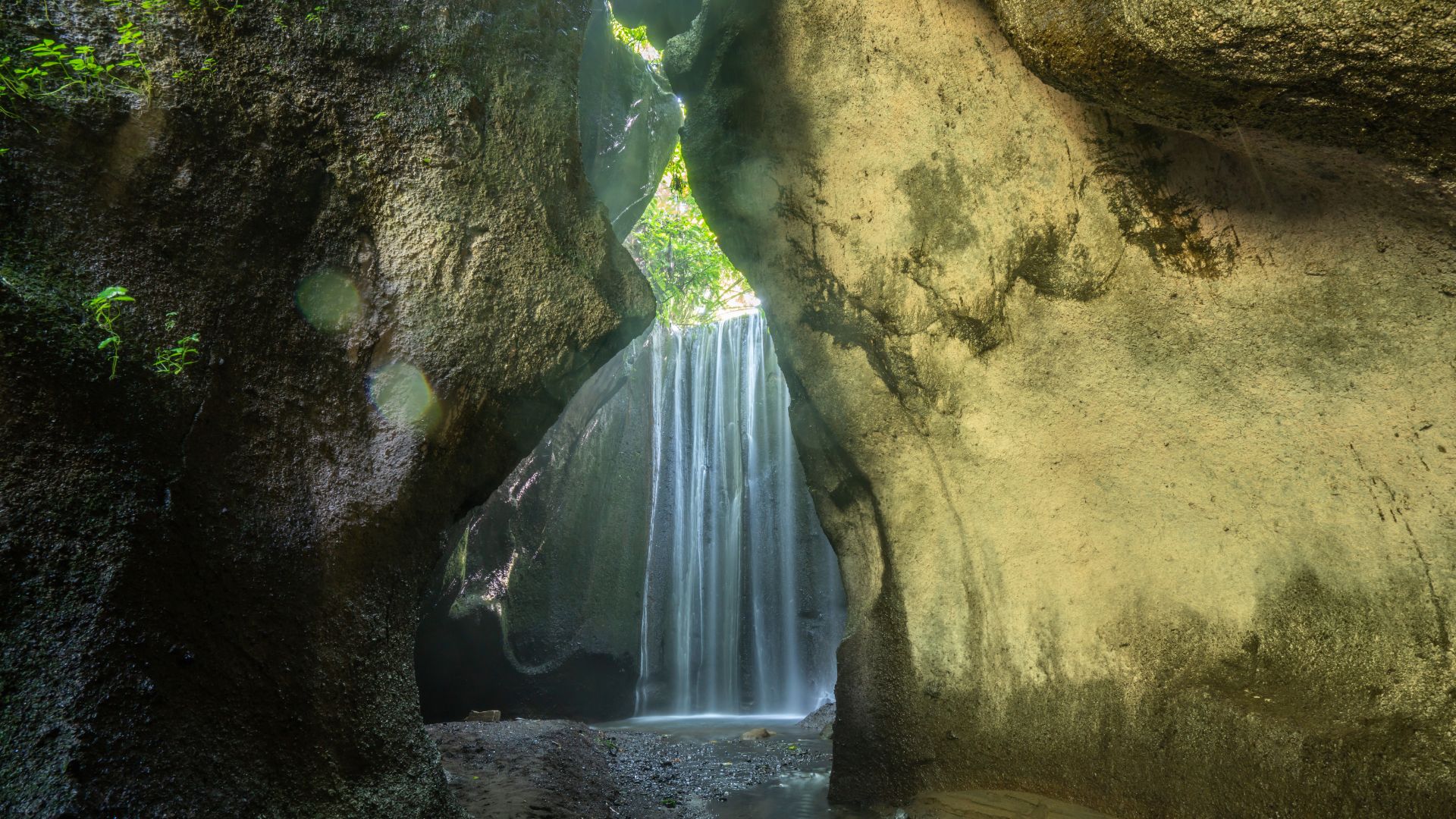 Tukad Cepung Waterfall in Bali flows through a cave-like opening with sunlight streaming in. The hidden spot feels magical and peaceful for visitors.